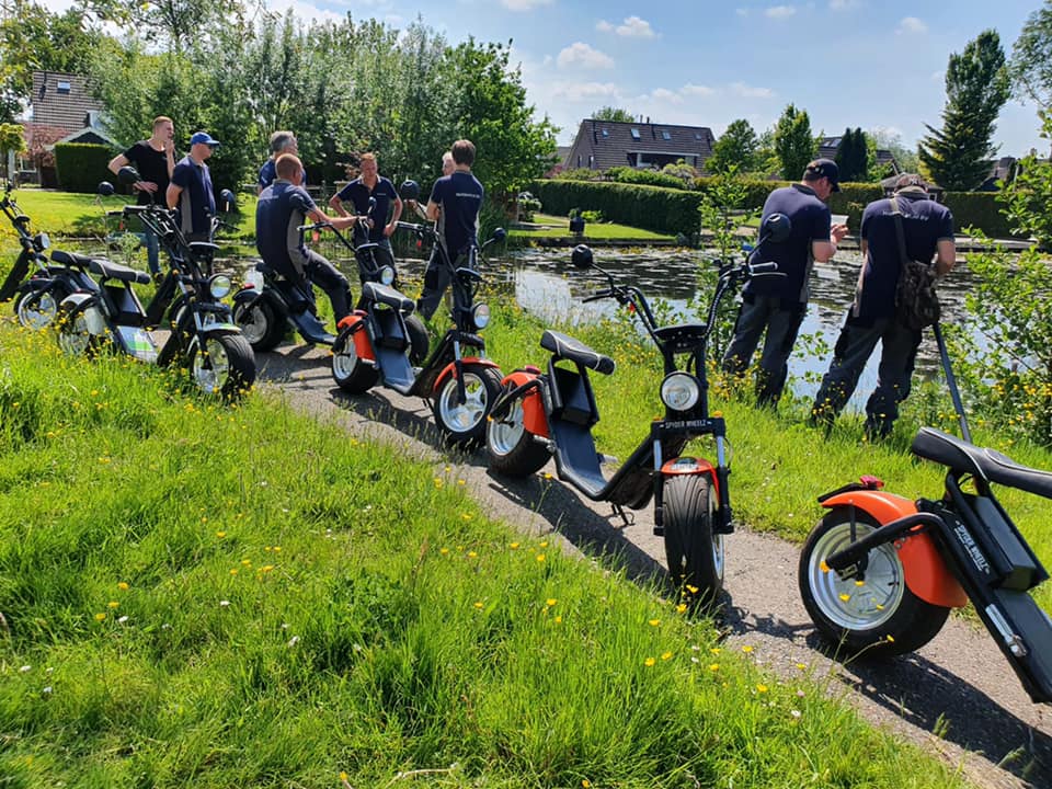 Geparkeerde e-choppers op een pad langs het water, met een groep deelnemers erbij