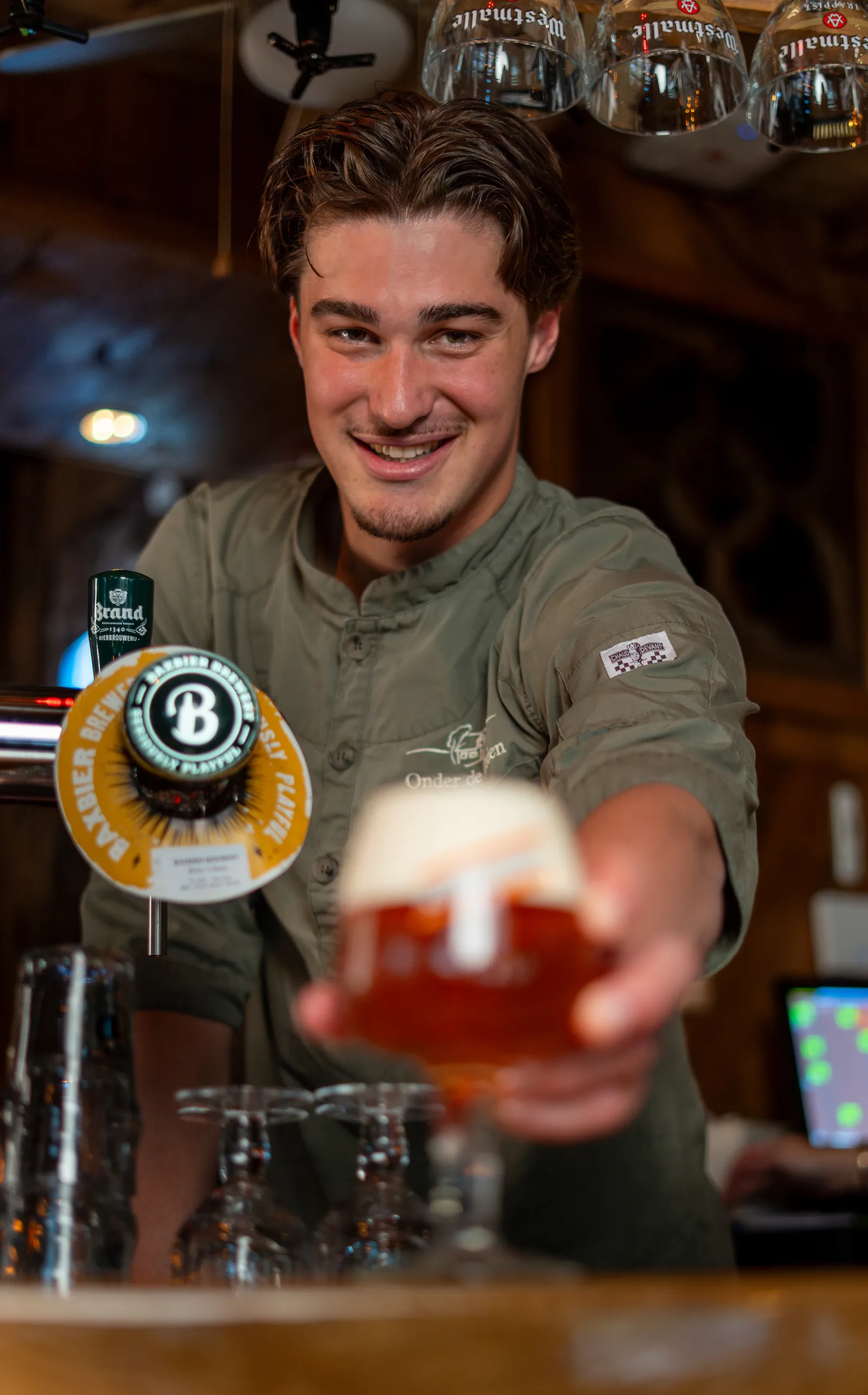 Lachende collega achter de tap reikt een glas speciaalbier over de bar aan