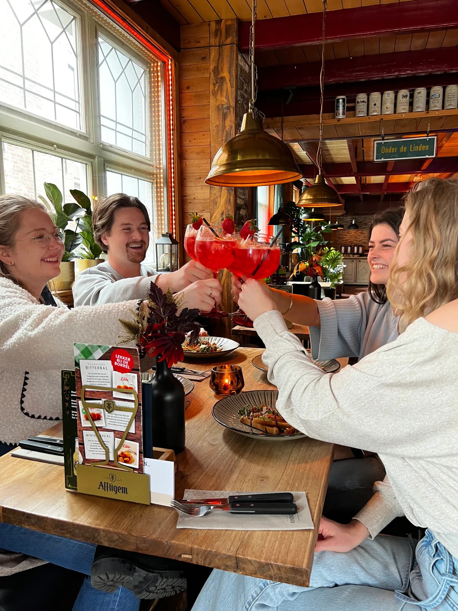 Vier gasten proosten aan tafel met grote rode cocktails in coupeglazen