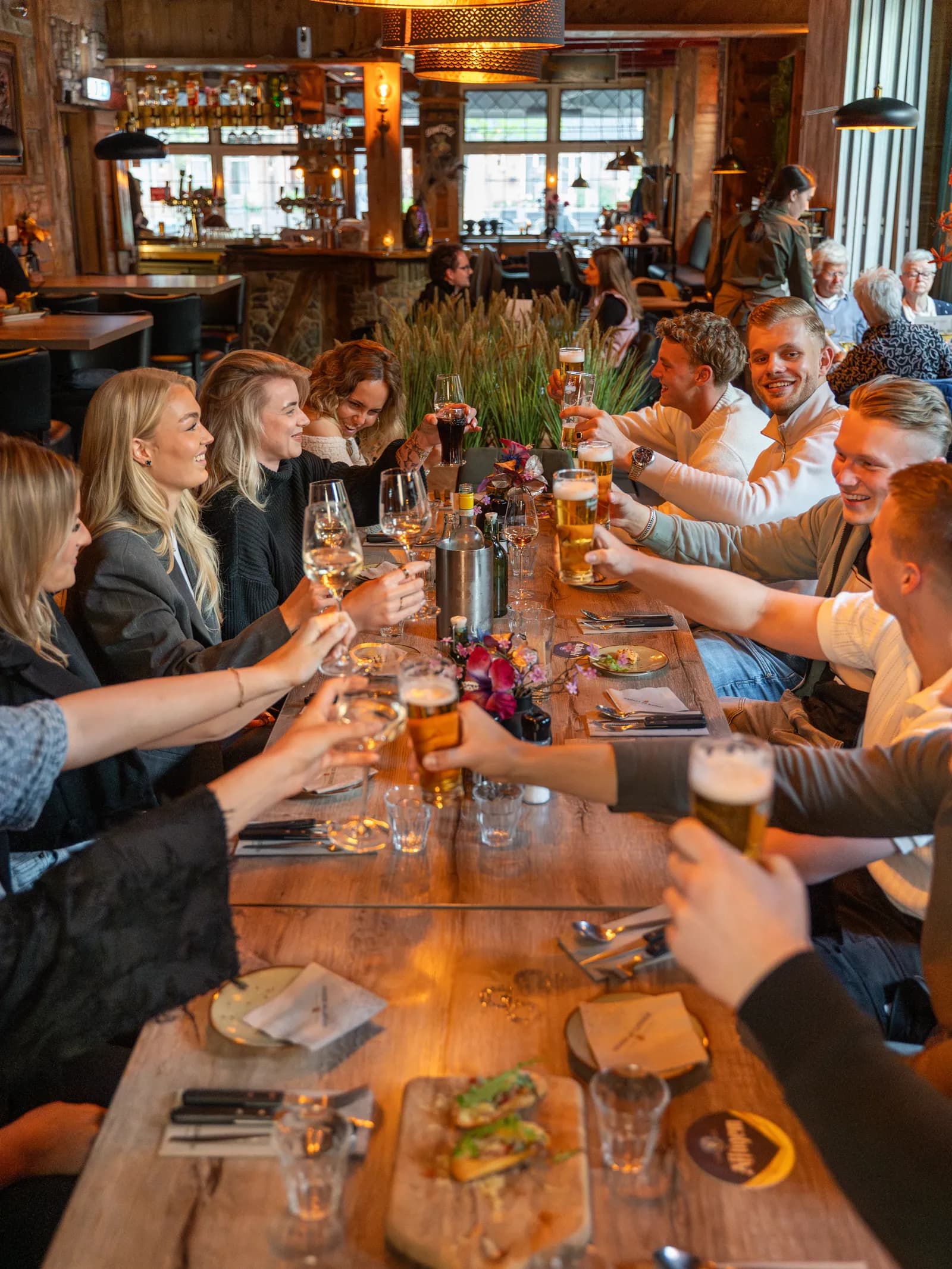 Gezelschap proost met bier en wijn aan de lange tafel in de gastrobar in Roden