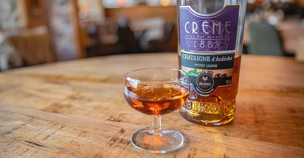 Glaasje kastanjelikeur naast de fles op een houten tafel