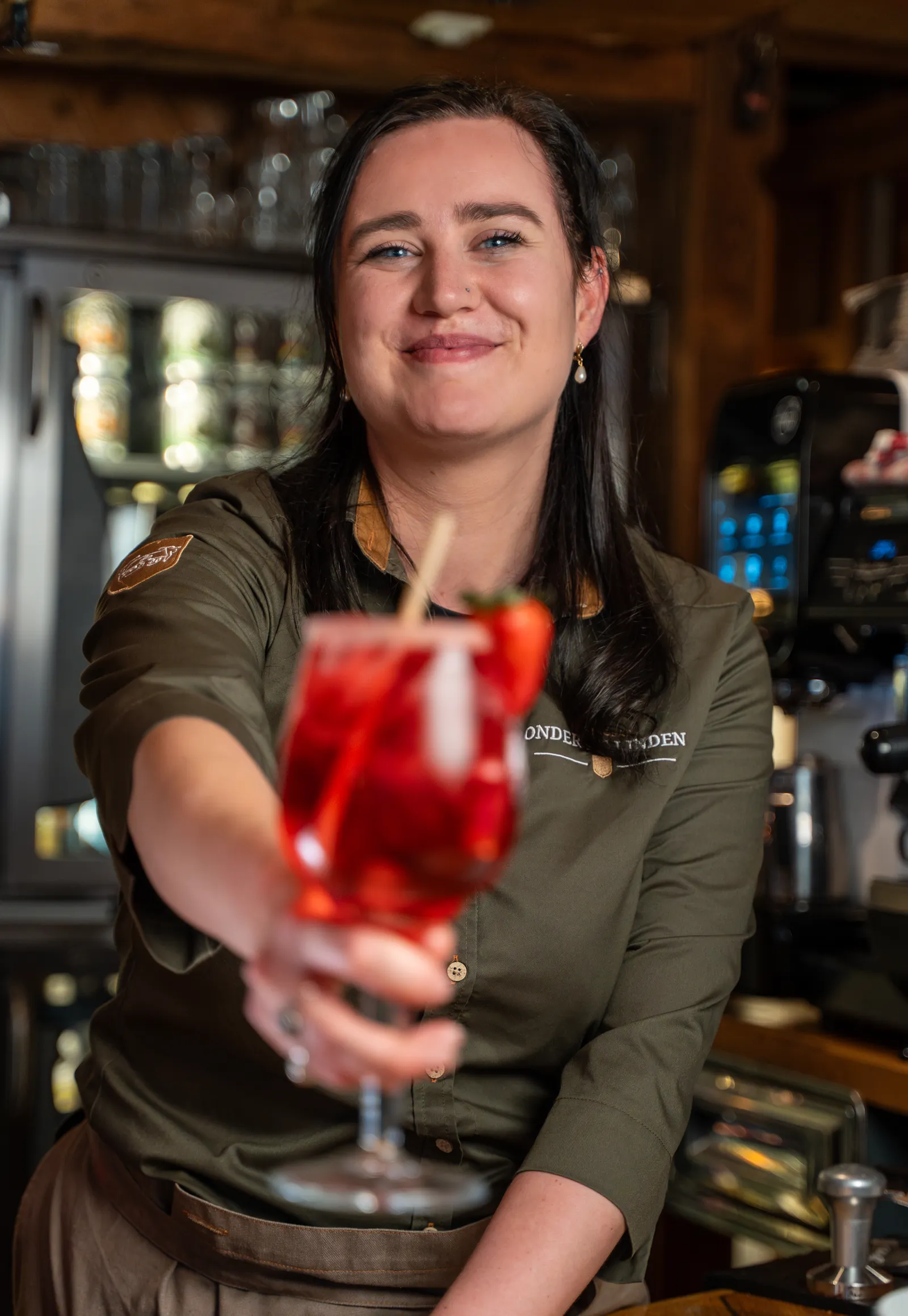 Lachende medewerkster reikt een cocktail met verse aardbei aan over de bar