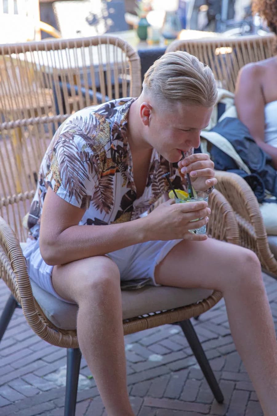 Jongeman drinkt een cocktail in een rieten stoel in de avondzon