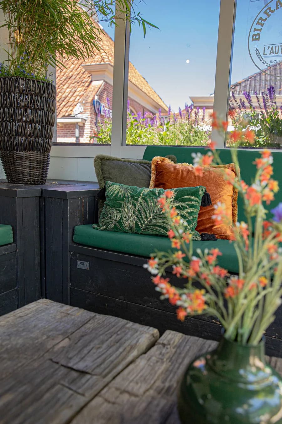 Loungebank met groene en okerkleurige kussens bij het raam van het terras