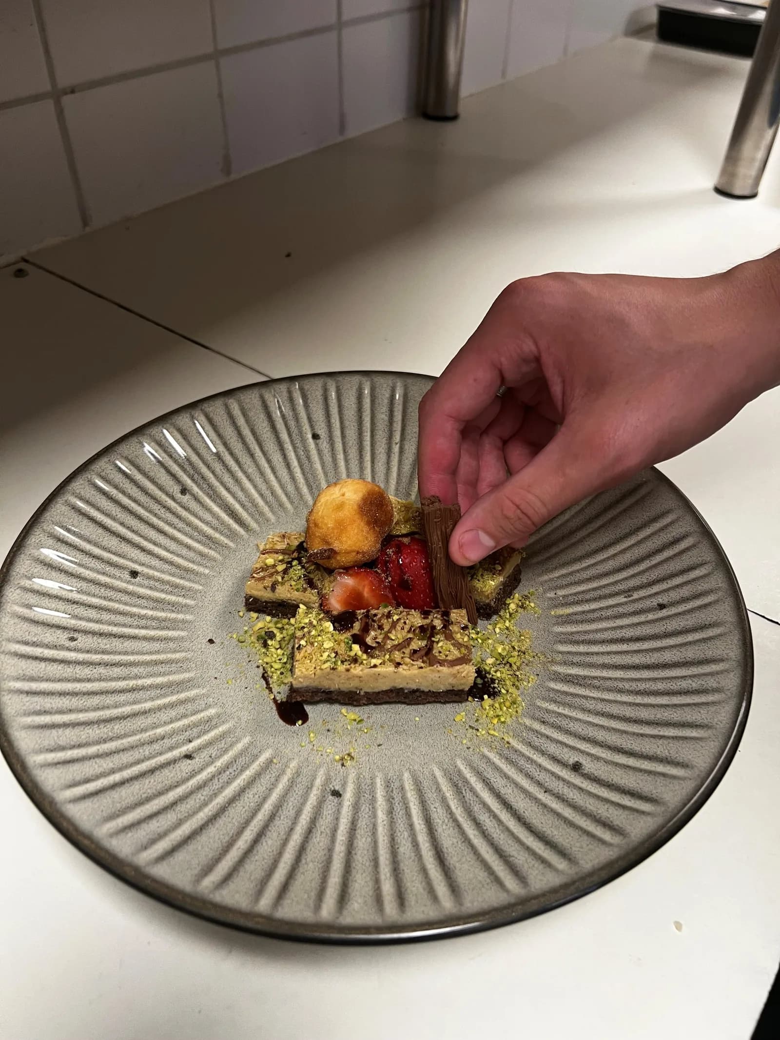 Dessert met pistache, aardbei, chocolade en een soesje wordt op een geribbeld bord afgemaakt