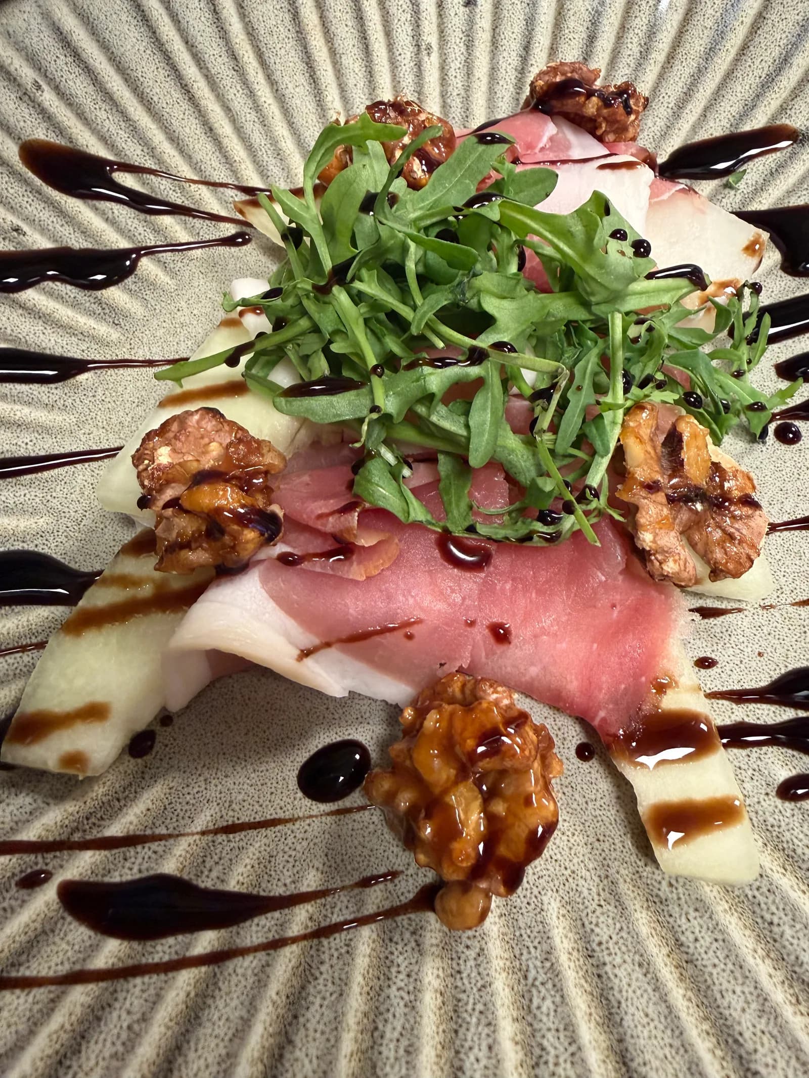 Voorgerecht met ham van Flap, meloen, rucola, gesuikerde walnoot en balsamico op een geribbeld bord