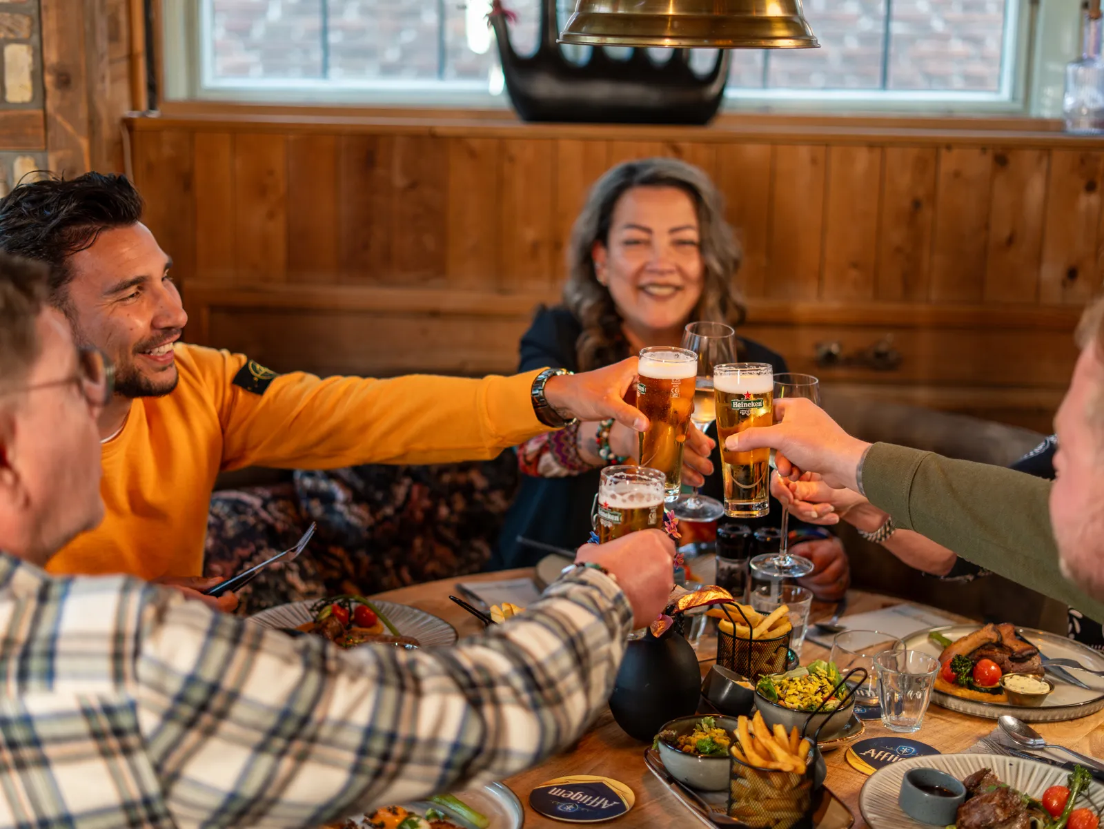 Gezelschap proost met bier aan een tafel vol gerechten met friet en salade