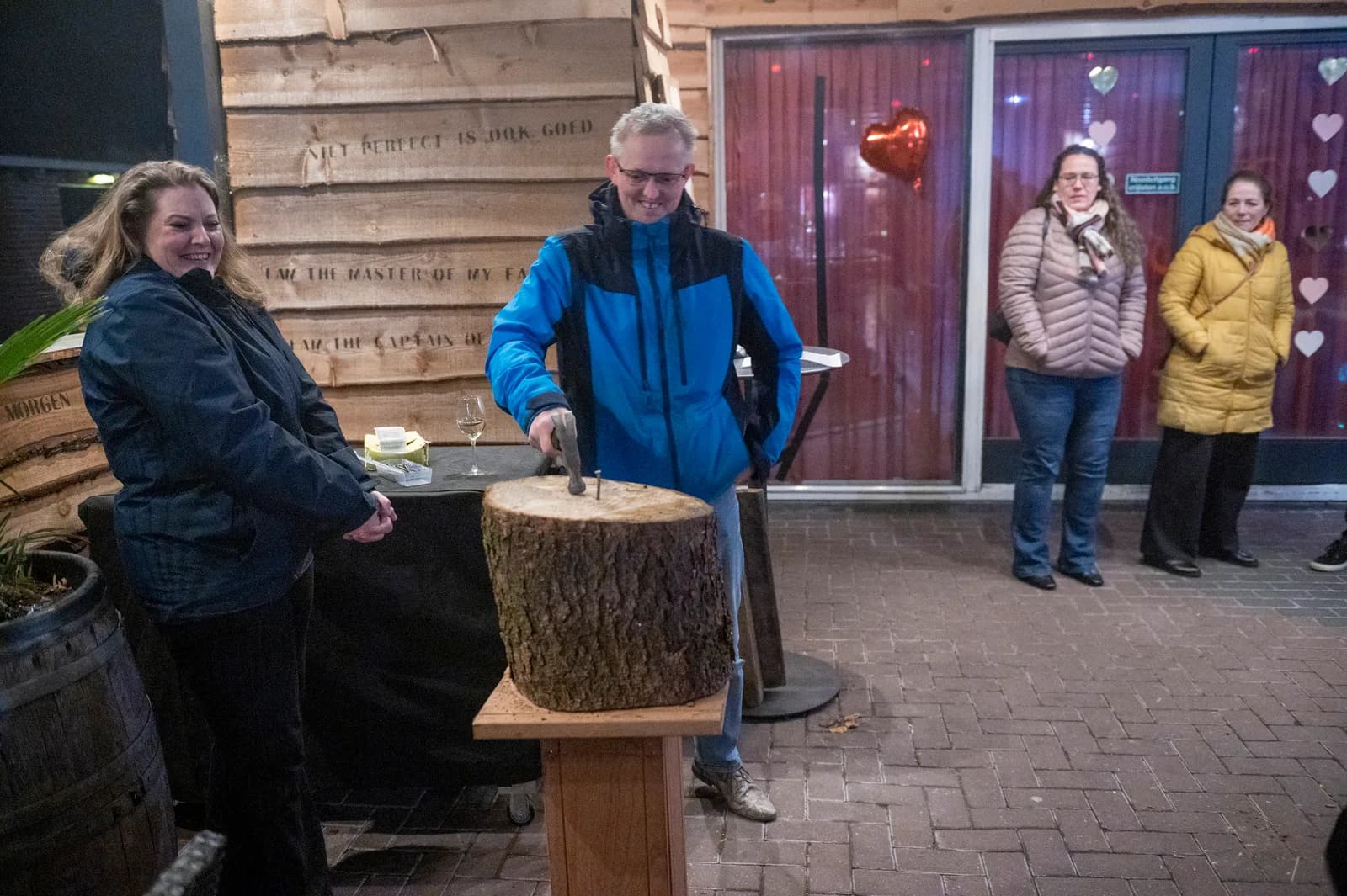 Deelnemer slaat een spijker in een boomstam terwijl de groep toekijkt