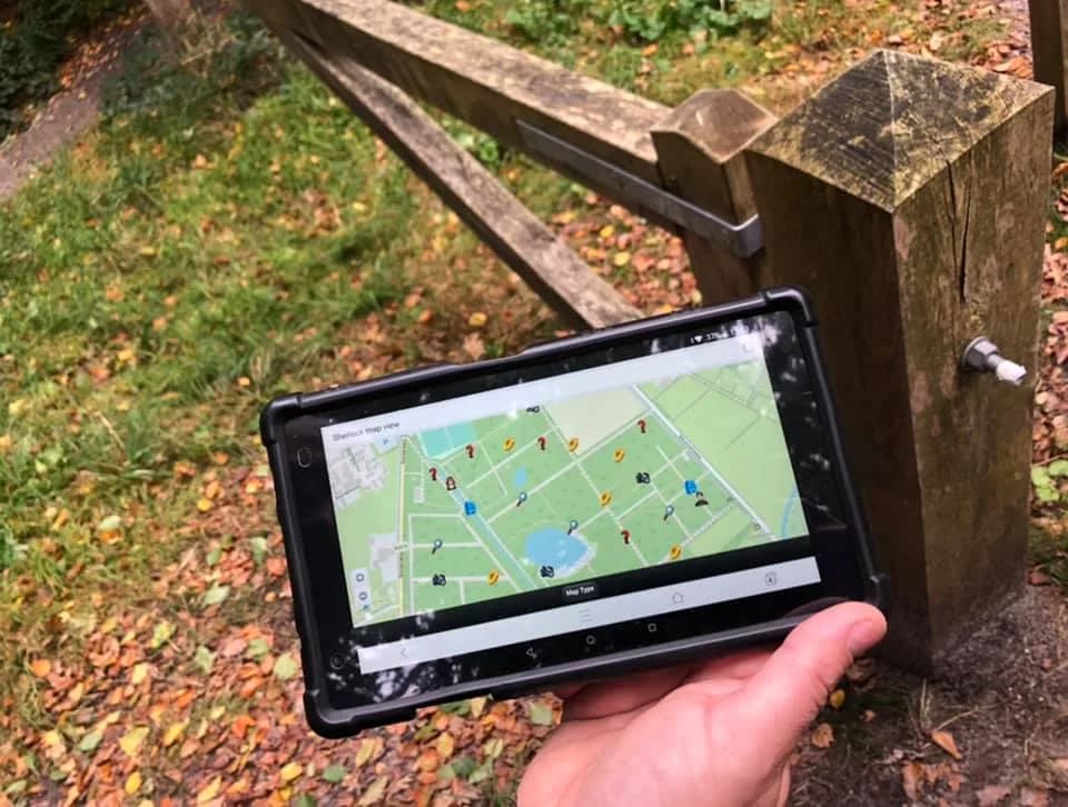 Tablet met de speurkaart van het spel, vastgehouden bij een hek in het bos