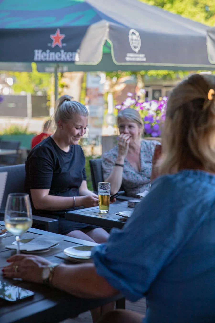 Lachende dames met bier aan tafel onder de parasol