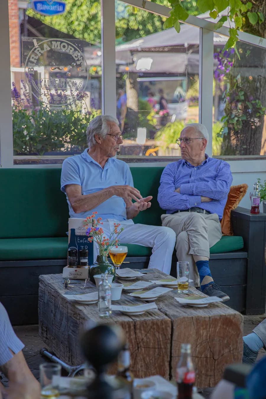 Twee heren in gesprek met bier op de groene terrasbank