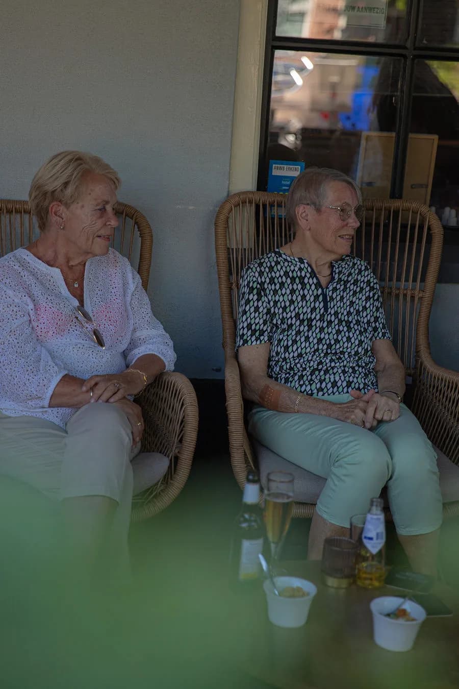 Twee dames met bubbels en kleine gerechtjes in rieten stoelen op het terras