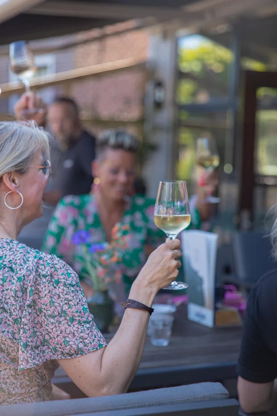 Gast heft een glas witte wijn op het terras