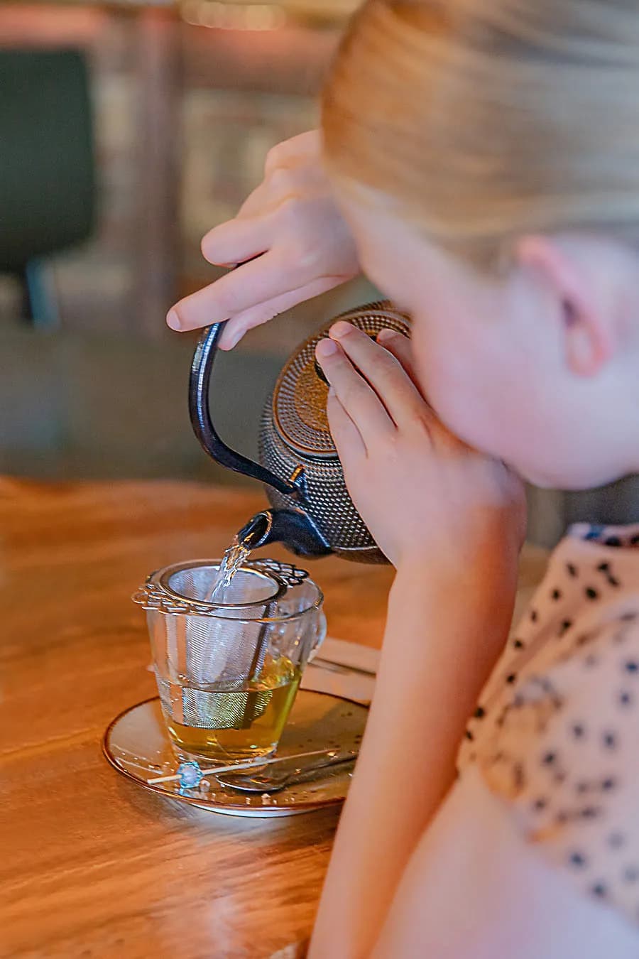 Meisje schenkt thee door een zeefje in een glas