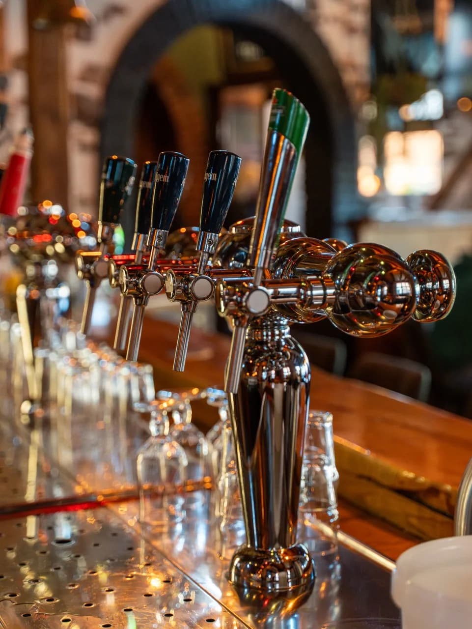 Chromen biertaps op de bar met omgekeerde glazen ervoor en een gemetselde boog erachter