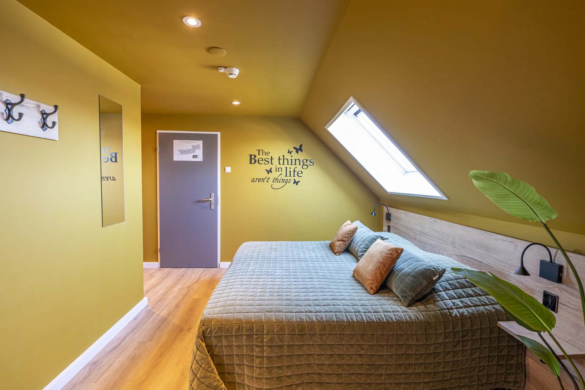 Hotelkamer met dakraam en de muurtekst The best things in life aren’t things