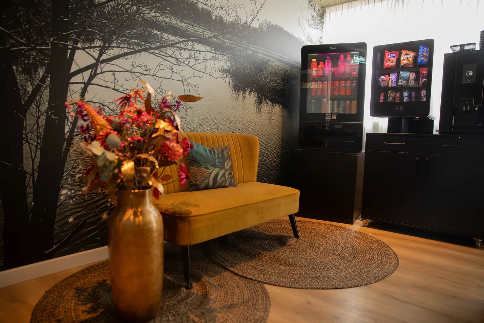 Gele bank met droogbloemen op de hotelgang, naast de koffiemachine en de koelkast met drankjes