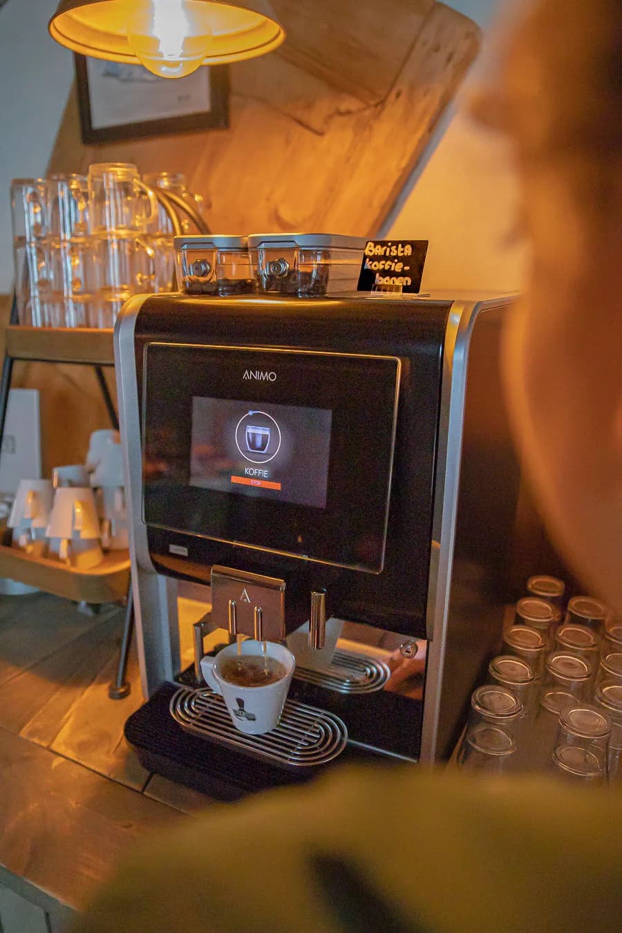 Koffieautomaat op de hotelgang met glazen, kopjes en een bordje barista-koffiebonen