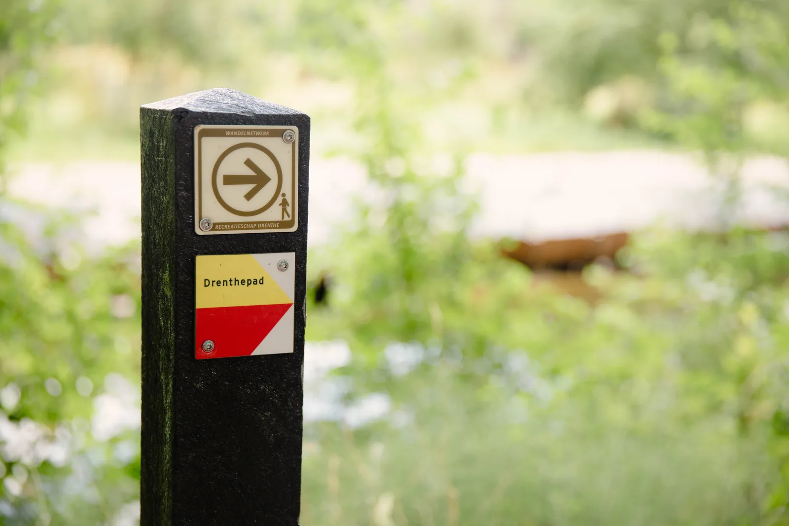 Zwart routepaaltje met een bordje Drenthepad en een pijl met wandelaarpictogram