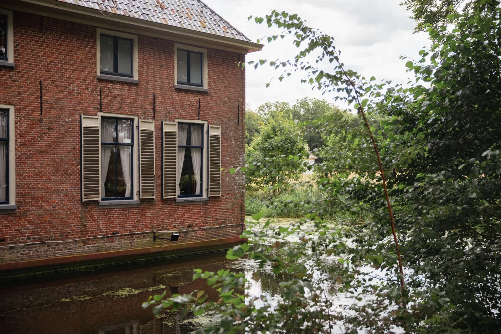 Bakstenen havezate met luiken, pal aan de gracht van Landgoed Mensinge