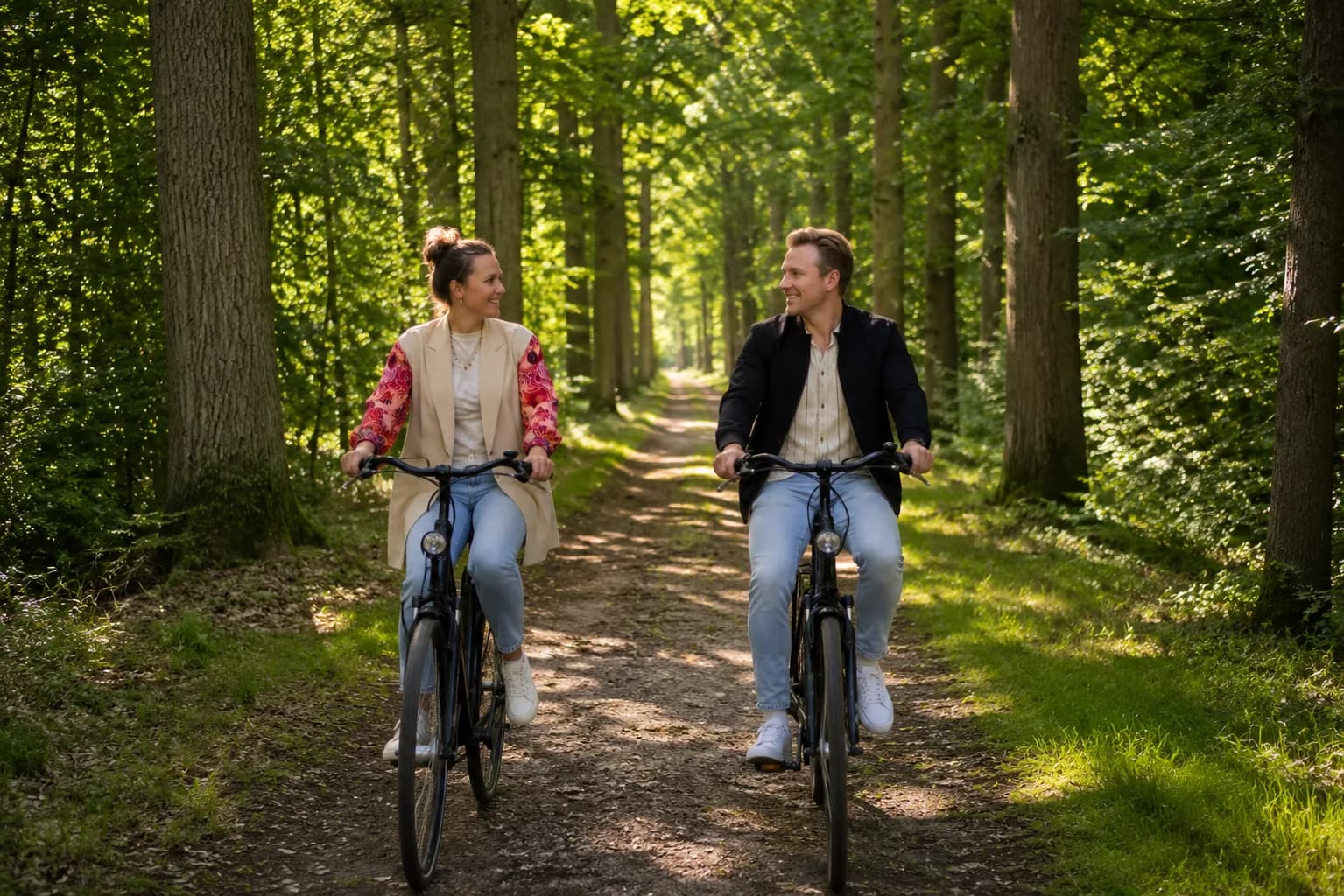 Stel fietst naast elkaar over een zandpad door een zonnige beukenlaan