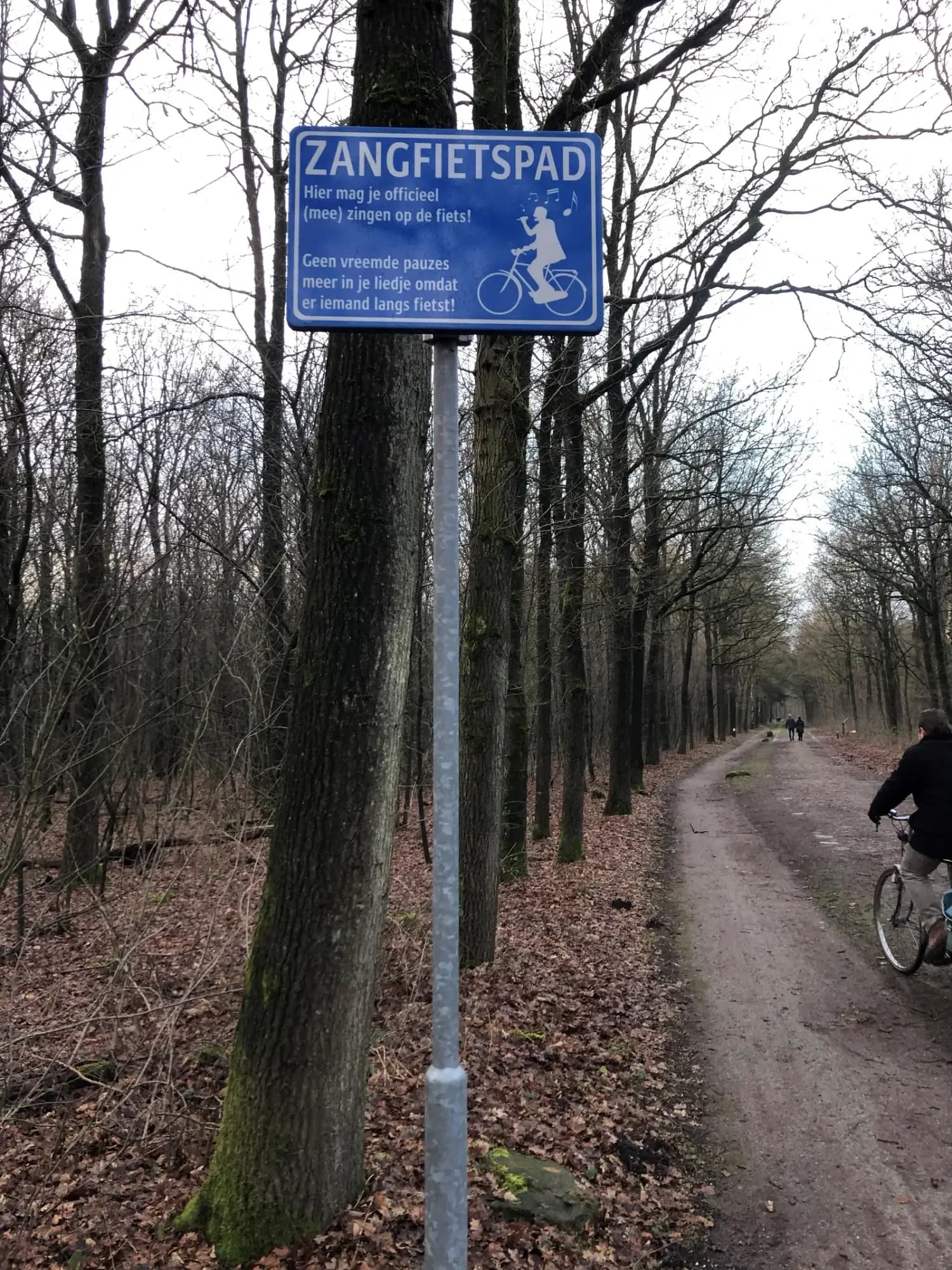 Bord Zangfietspad langs een bospad, met een fietser op het pad