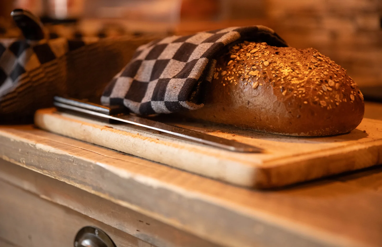 Meergranenbrood met zaden in een geblokte doek op een houten snijplank, met broodmes