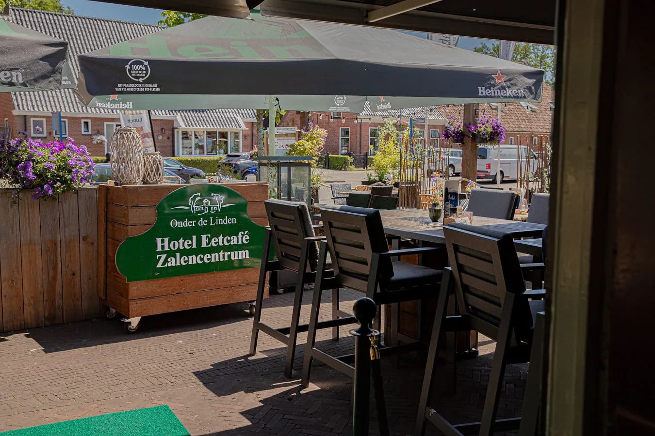Het terras van Onder de Linden aan de Brink in Roden, met het naambord en gedekte tafels onder de parasol