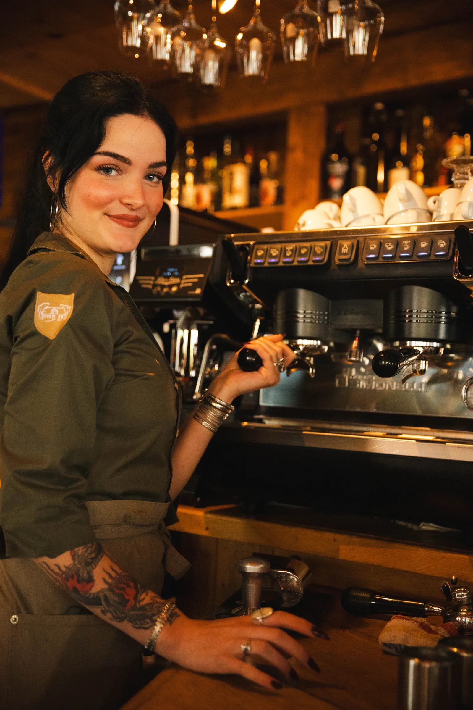 Collega bedient de espressomachine achter de bar, met kopjes klaar op de machine