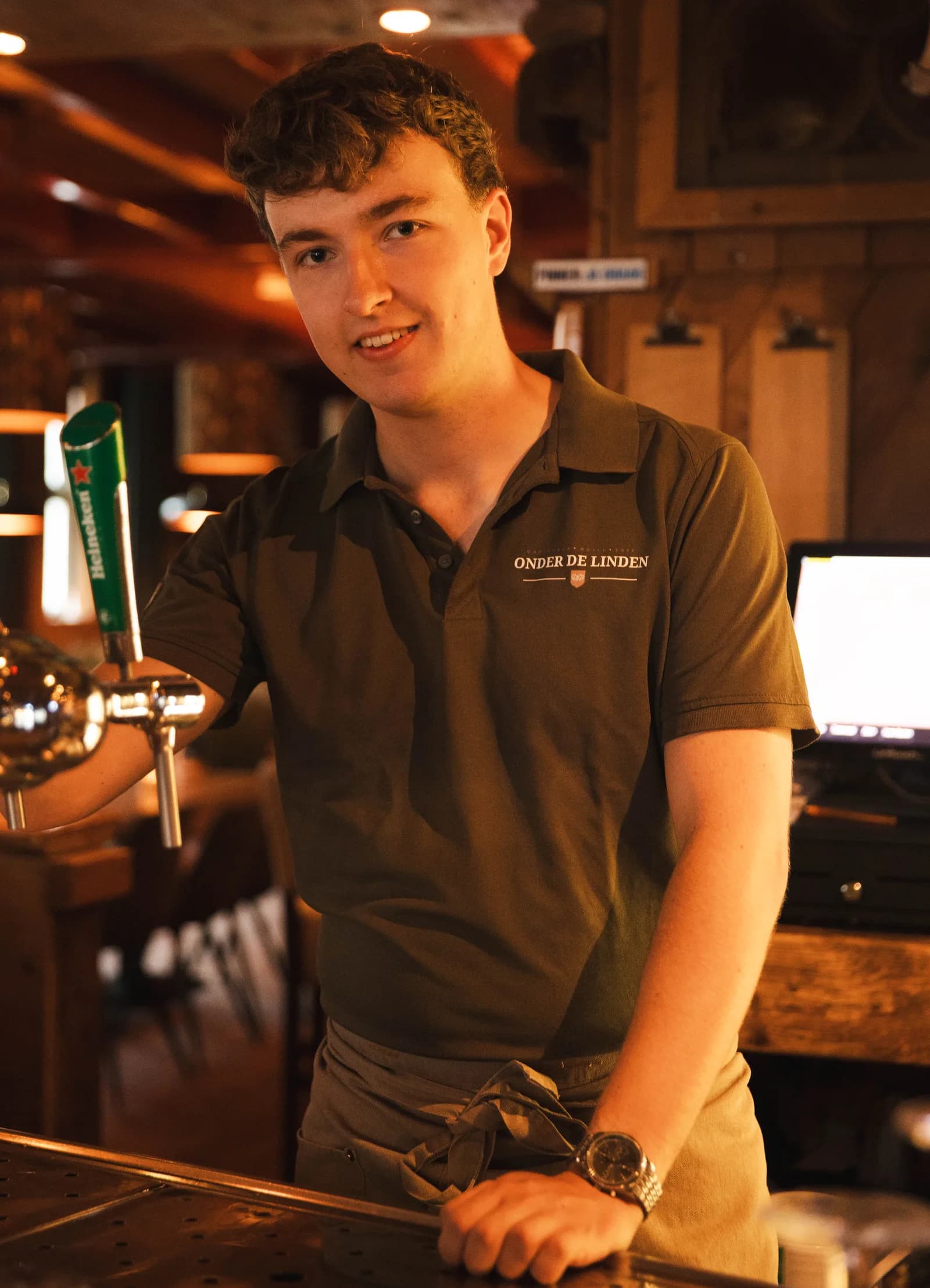 Collega staat aan de Heineken-tap achter de bar en kijkt in de camera