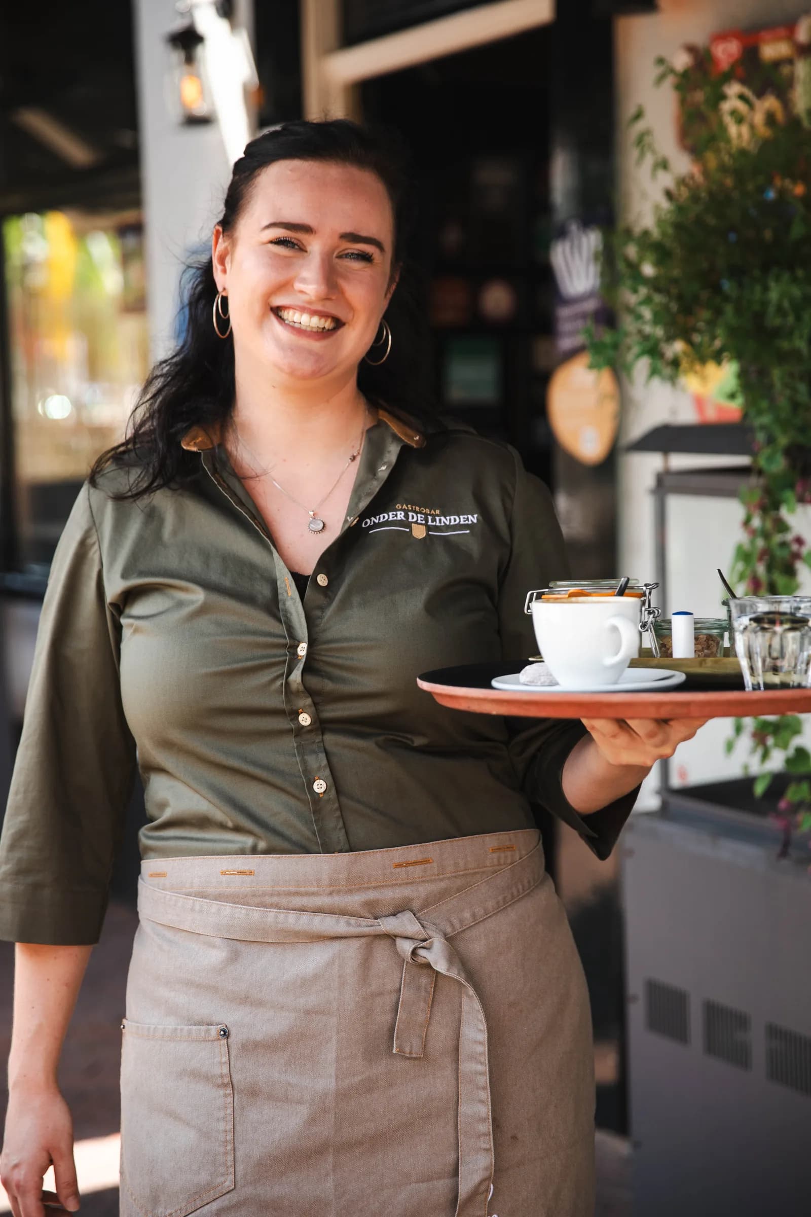 Lachende medewerkster draagt een dienblad met koffie en water naar het terras