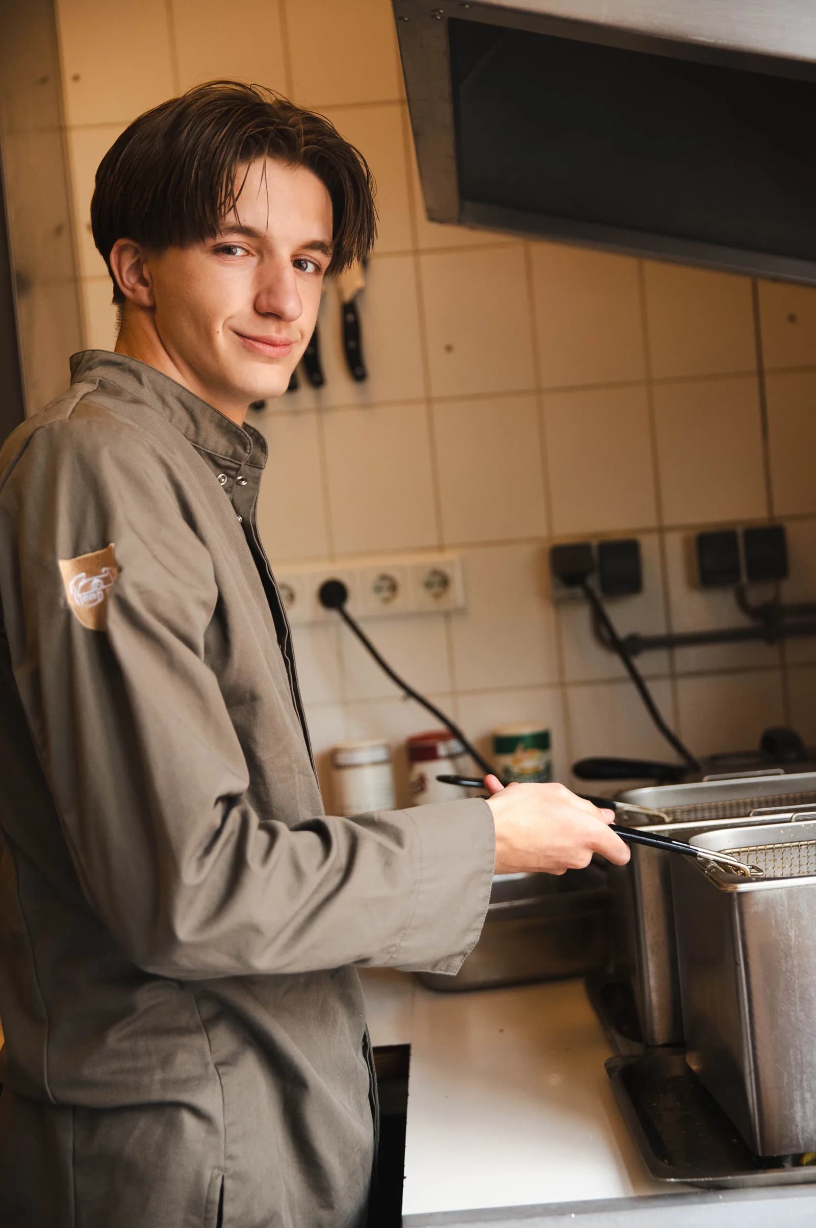 Kok in olijfgroen koksbuis tilt de frituurmand op in de keuken