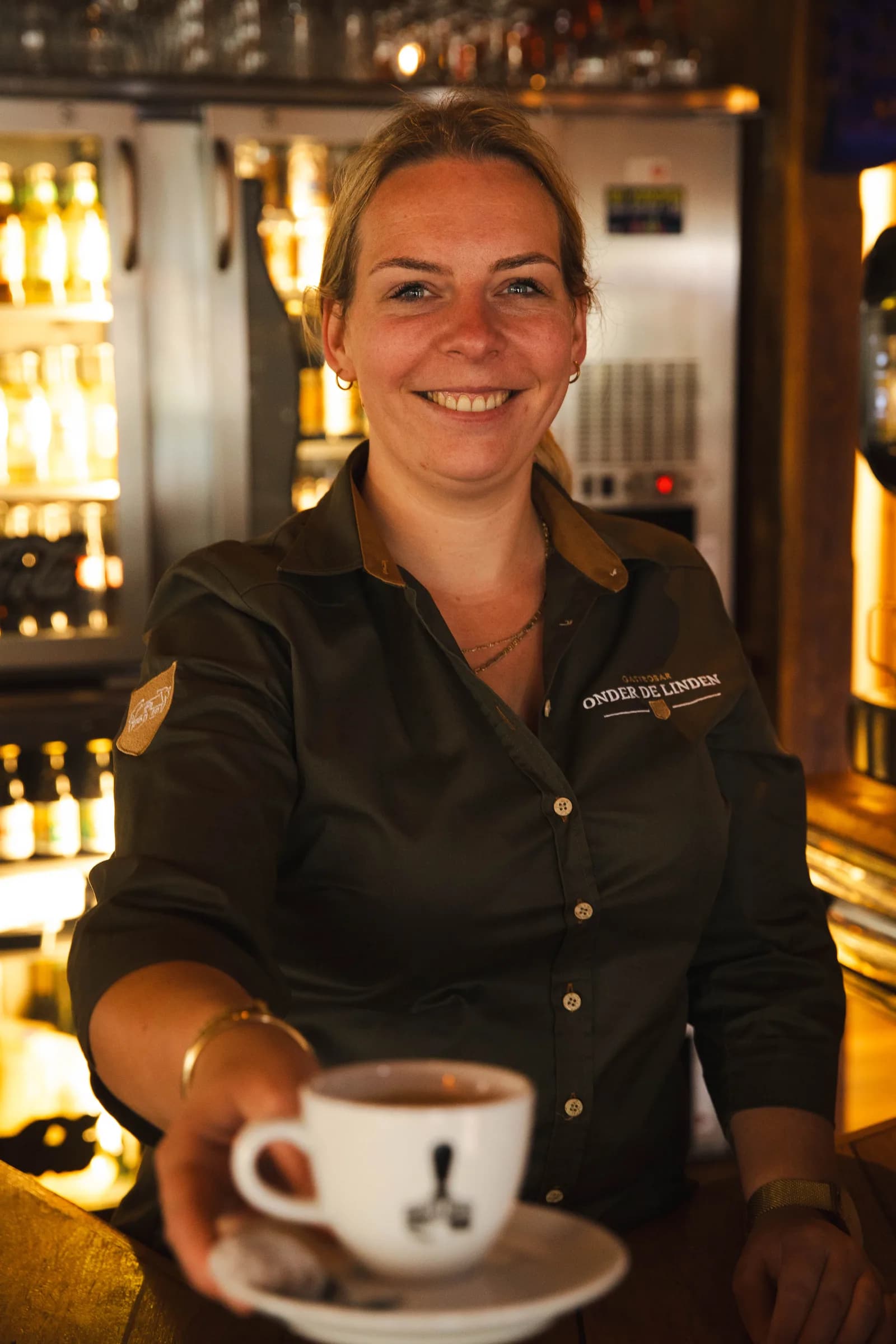 Lachende medewerkster reikt een kop koffie op een schotel over de bar aan