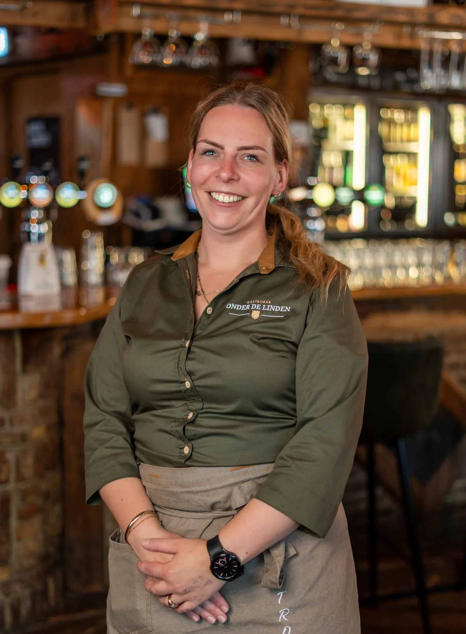Lachende medewerker in groene bedrijfskleding bij de bar