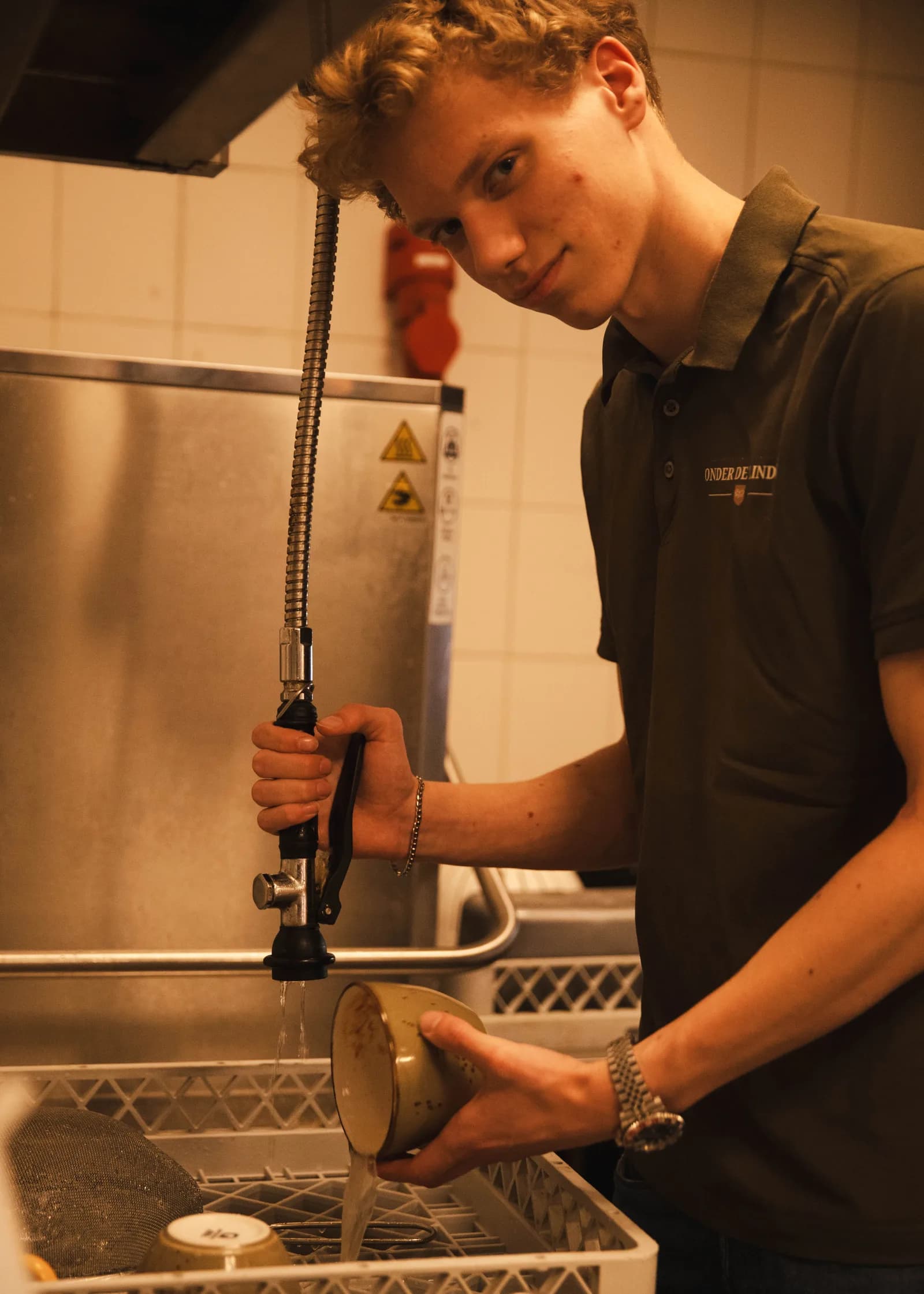 Collega spoelt serviesgoed af met de spoeldouche boven de vaatwaskorf