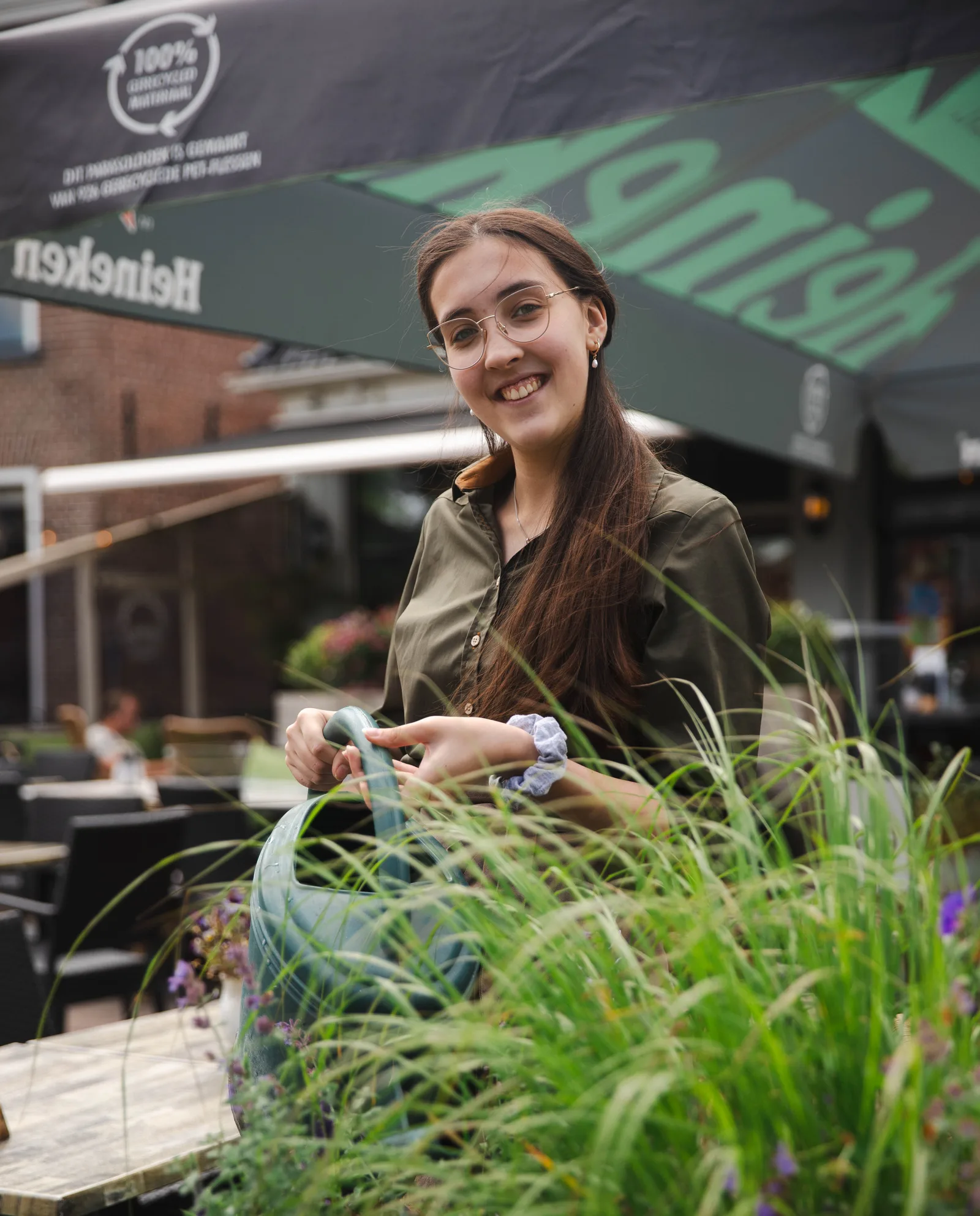 Lachende medewerkster geeft de planten in de bloembakken op het terras water met een gieter
