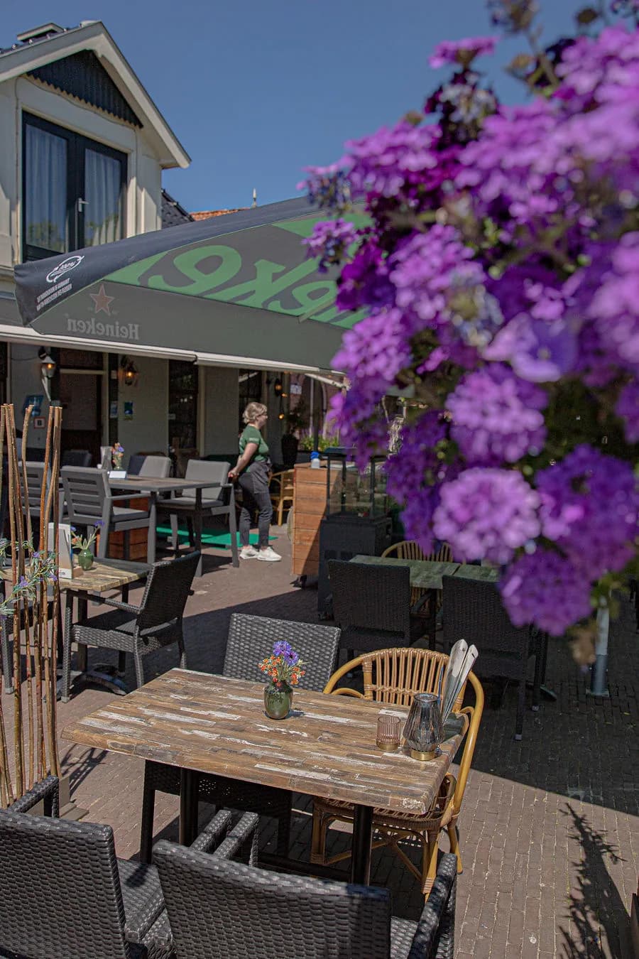 Terras met tafels onder paarse hangbloemen in de zon