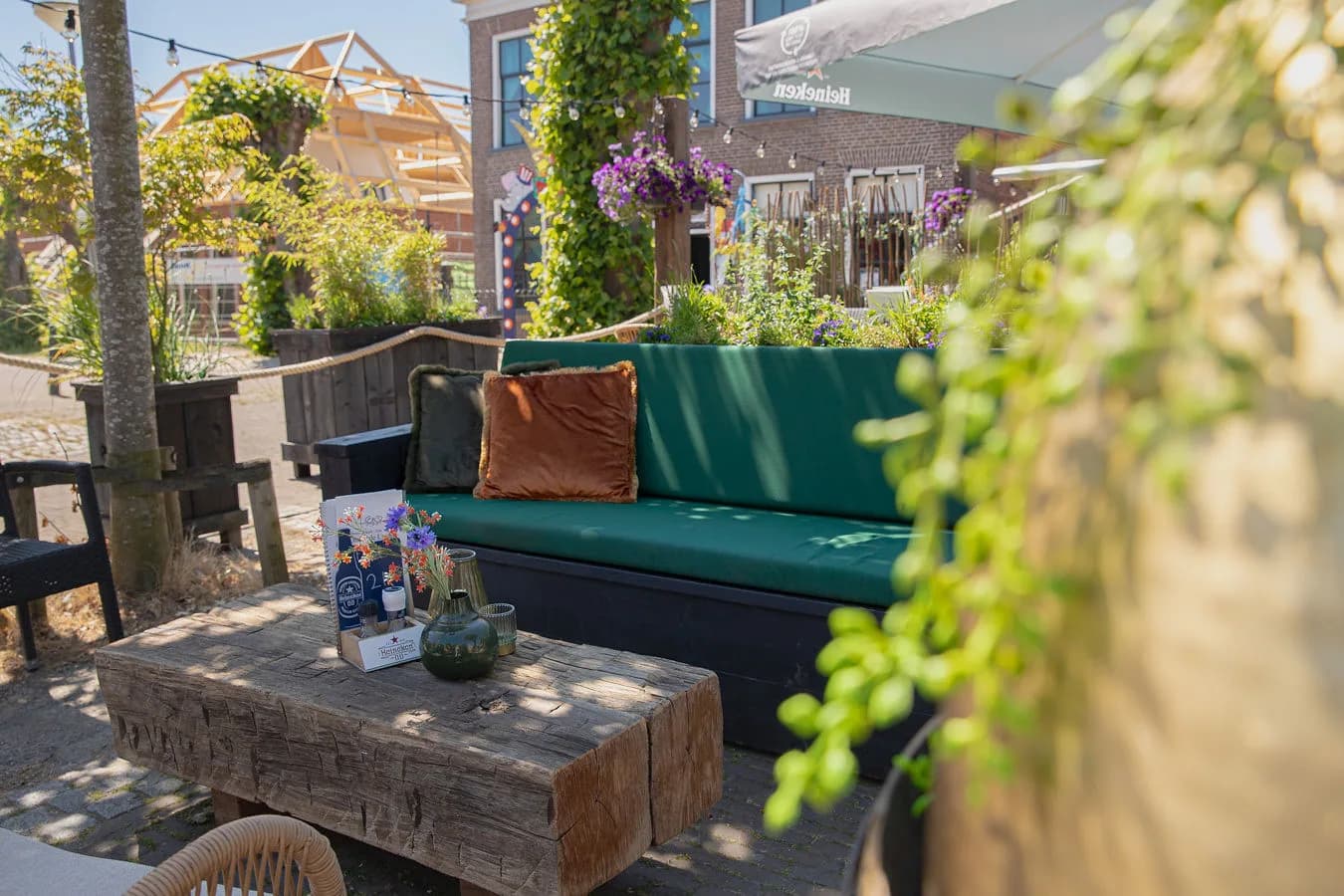 Loungehoek op het terras met een groene bank, kussens en een houten tafel met bloemen