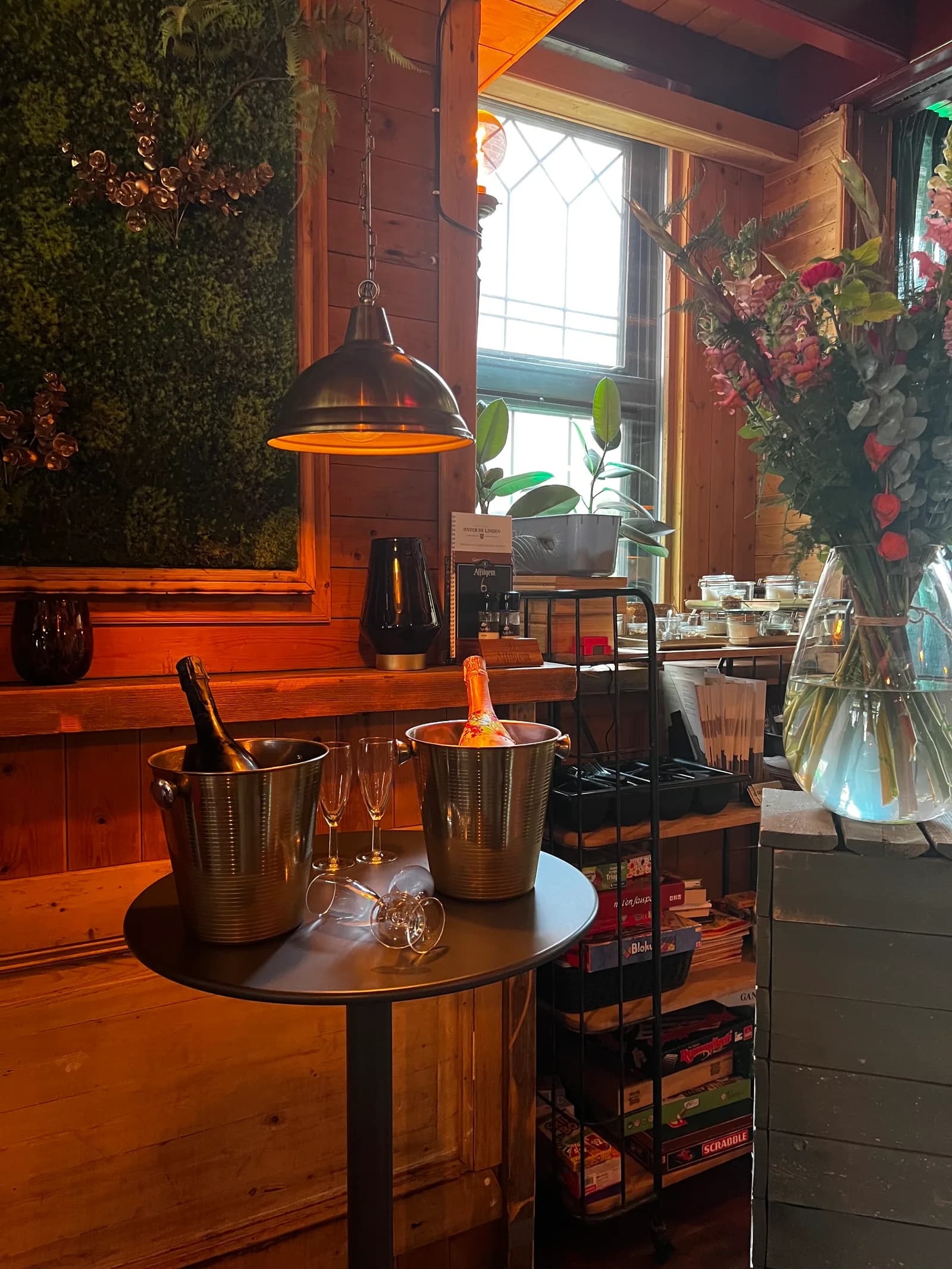 Twee flessen champagne in koelers op een statafel, met glazen en een hoog bloemstuk ernaast