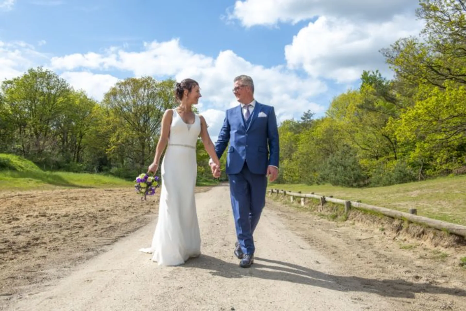 Bruidspaar wandelt hand in hand over een zandpad in Drenthe