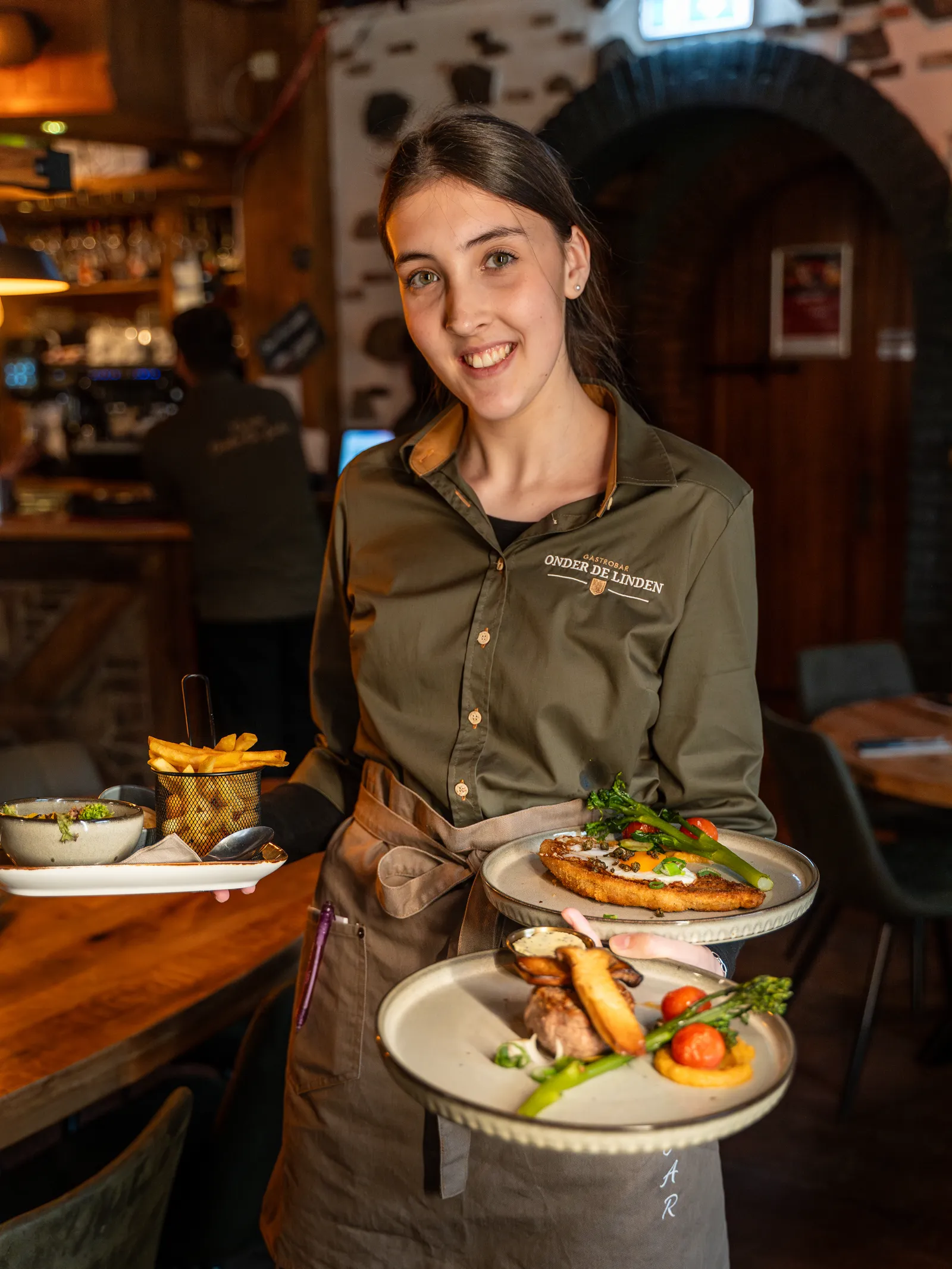 Lachende medewerkster draagt drie borden tegelijk door de gastrobar