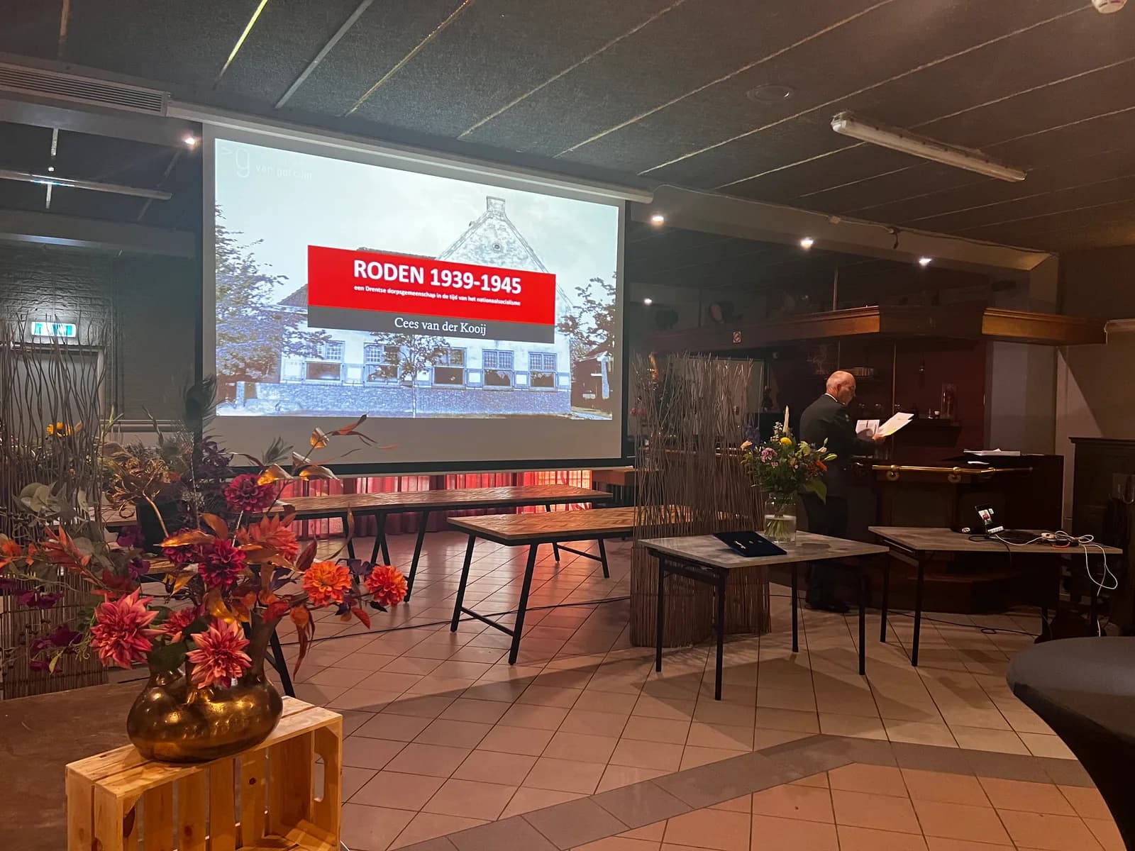 Boekpresentatie in de zaal: spreker bij een projectiescherm met de titel Roden 1939-1945