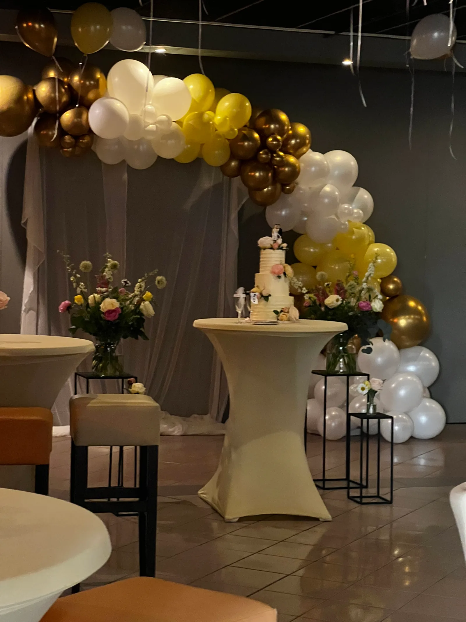 De bruidstaart tussen twee bloemstukken voor een gedrapeerde achterwand