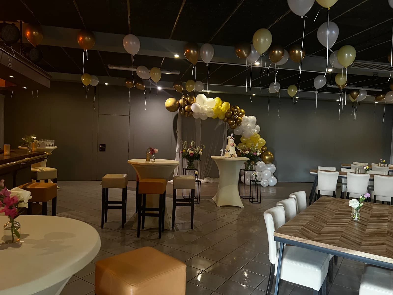 Zaal met ballonboog, gedekte tafel en statafels klaar voor de gasten