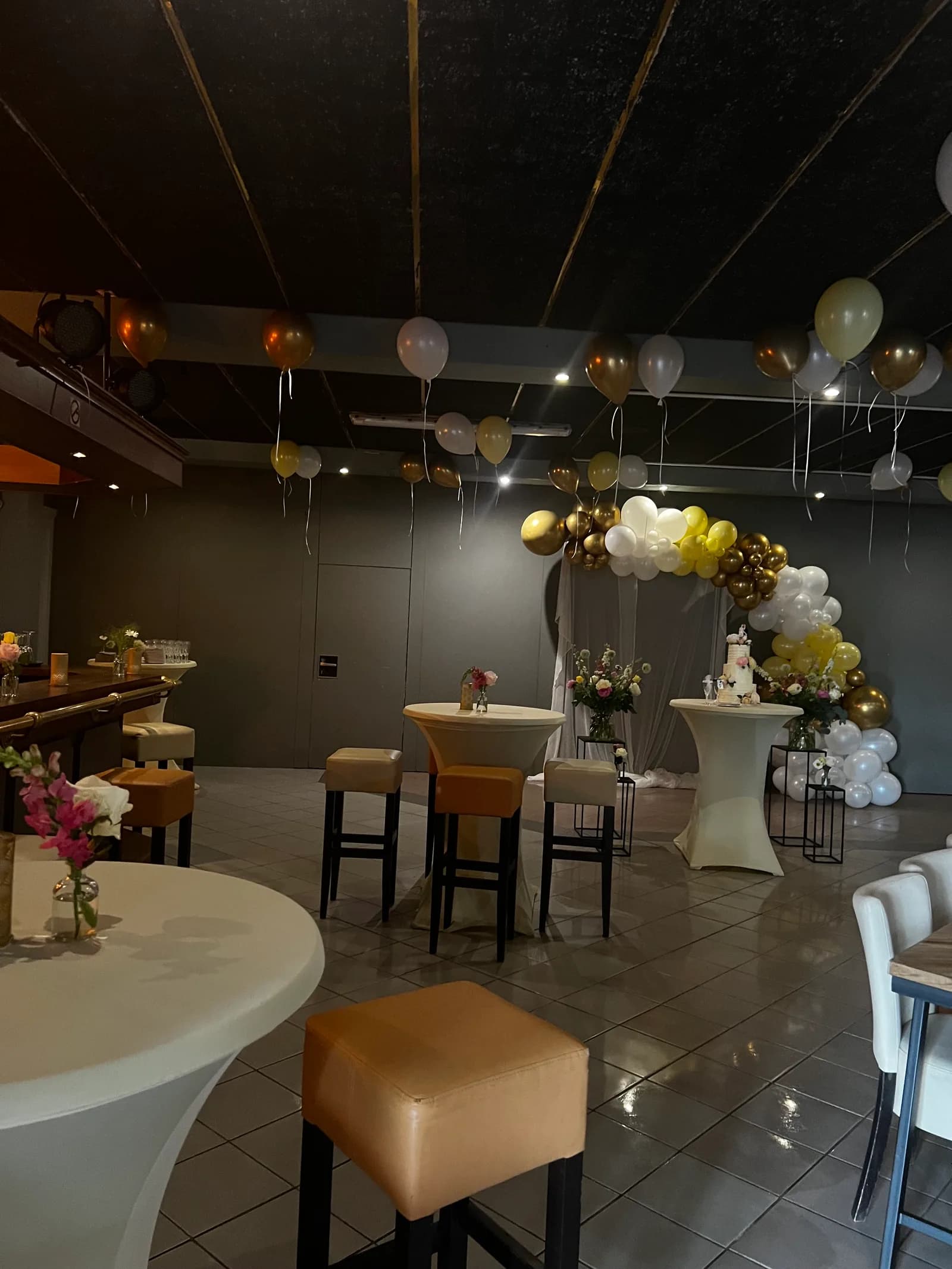 Overzicht van de zaal met zwevende ballonnen boven de statafels en de taart op de achtergrond