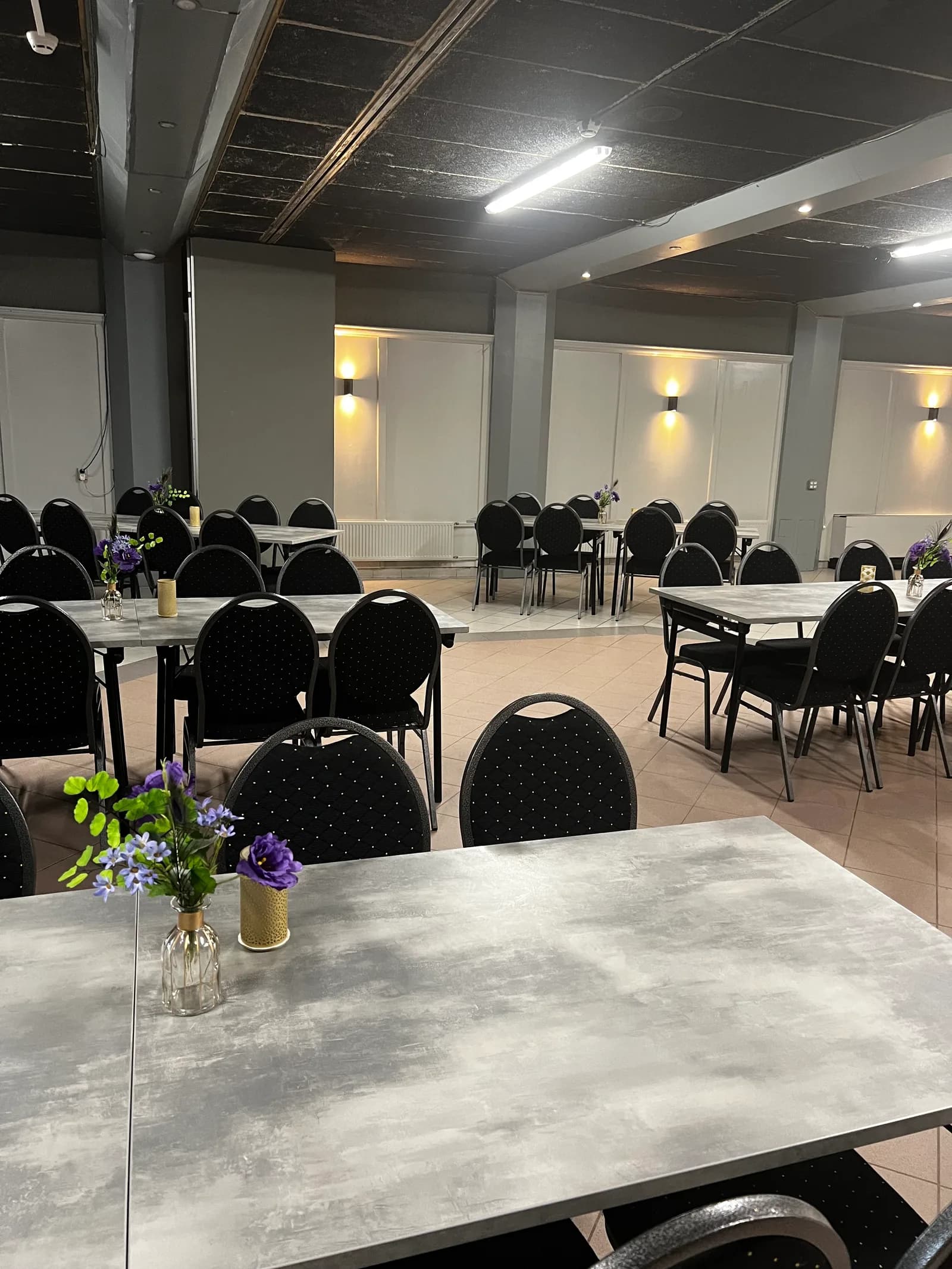 Gedekte tafels met paarse bloemen en zwarte stoelen, klaar voor een diner in de zaal