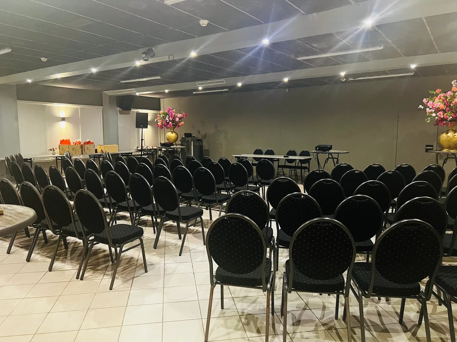Rijen stoelen gericht op een scherm en spreekgestoelte, met bloemstukken langs de zijkant