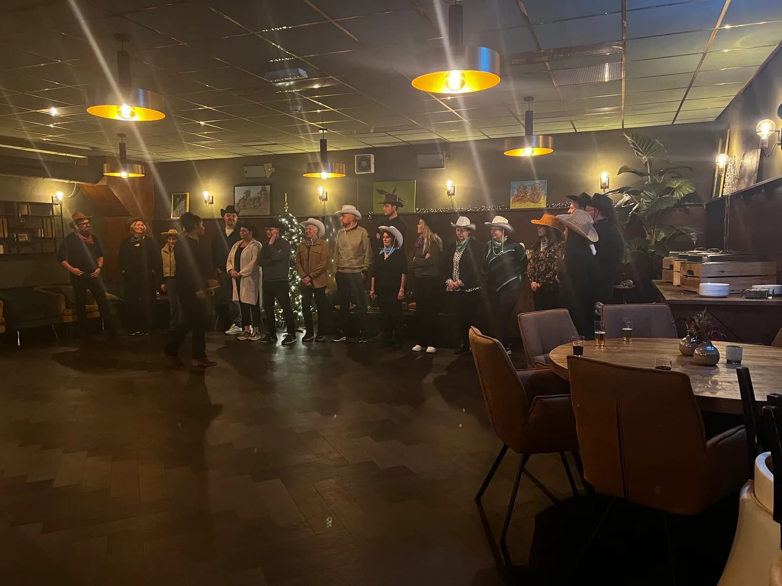 Gezelschap met cowboyhoeden staat opgesteld voor een groepsfoto tijdens een bedrijfsfeest in de zaal